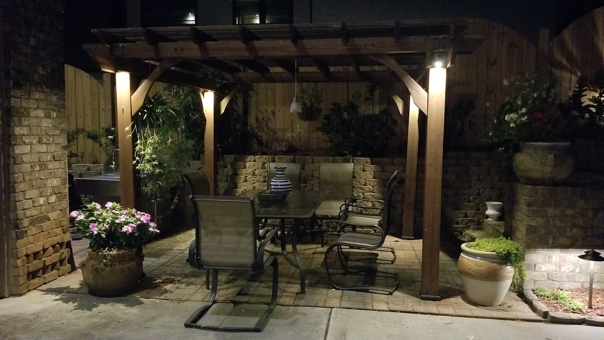 Premium solid brass down lights illuminating a luxury outdoor living space with comfortable seating, architectural woodwork, and landscape lighting.
